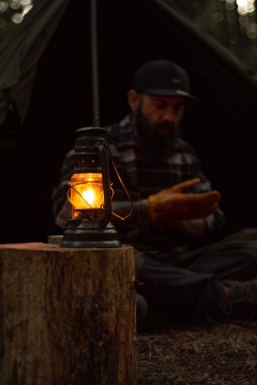 Free Moody outdoor scene with a camper warming hands near a glowing lantern. Stock Photo
