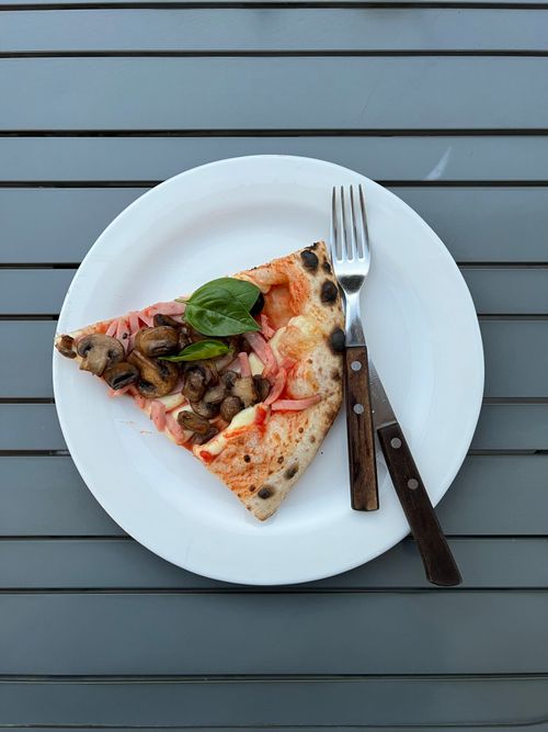 Free Overhead shot of a mushroom pizza slice on a white plate with utensils on a striped table. Stock Photo
