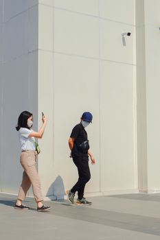 Two adults walking in an urban setting, wearing face masks under bright sunlight.