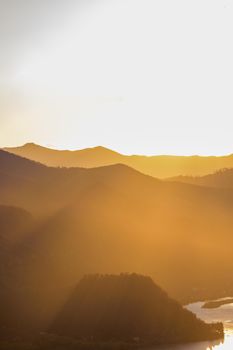 An aerial view of sunlit mountain ranges with mist during the golden hour.