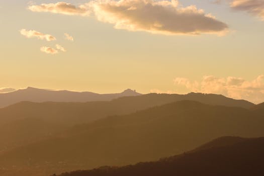 A tranquil view of layered mountains under a golden sky during sunset.