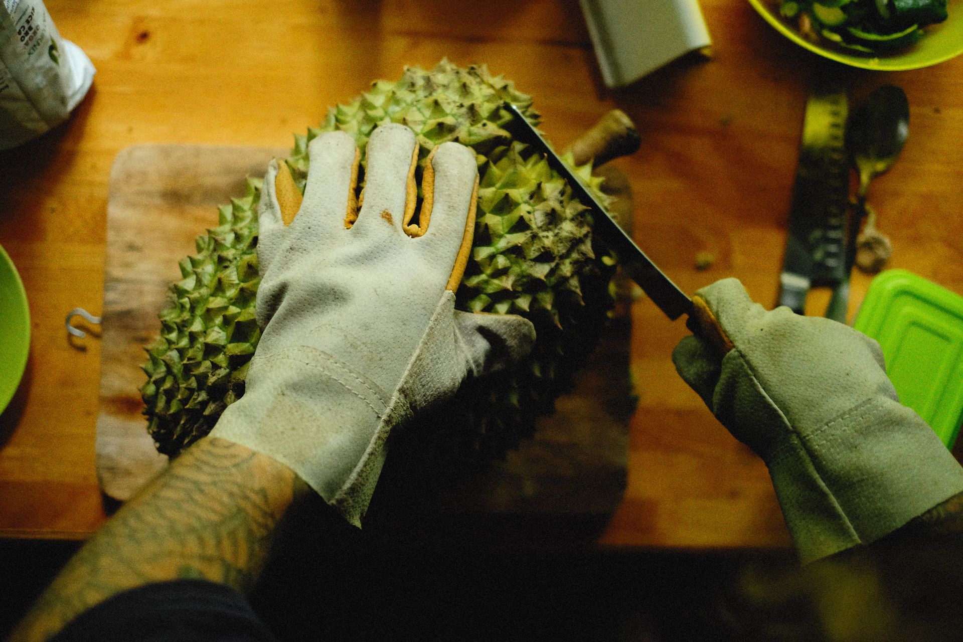 A close-up view of hands with gloves cutting a durian fruit on a wooden surface.