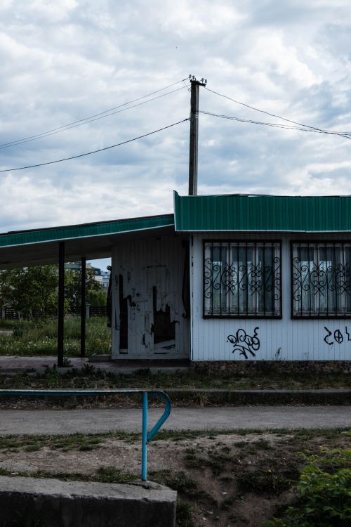Free An exterior view of a vandalized, abandoned shop with a green roof and barred windows under a cloudy sky. Stock Photo