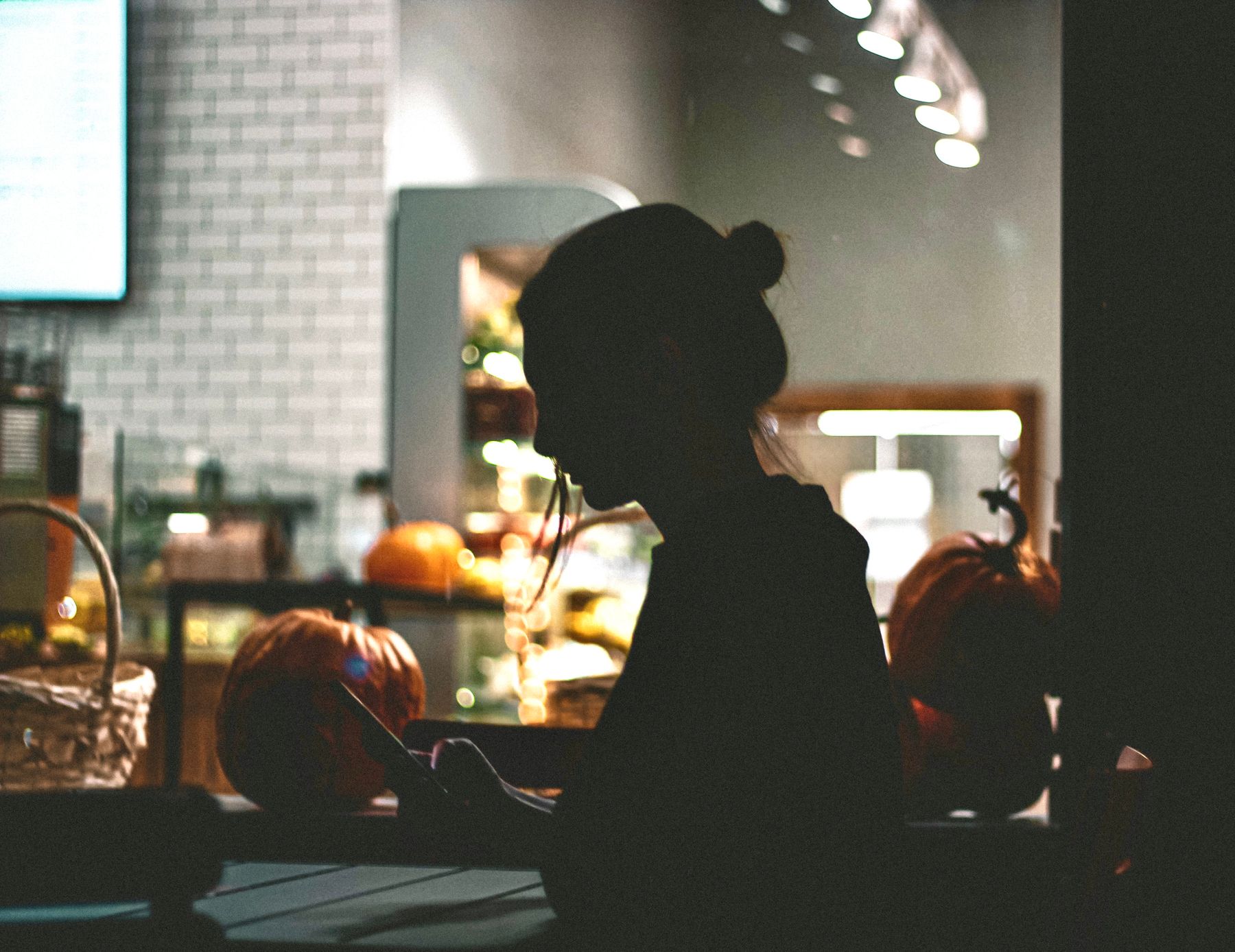 Silhouette of a woman using her phone in a warmly lit cafe — photo by Alexander Taranenko on Pexels