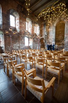 Interior of a historic venue with wooden chairs, brick walls, and elegant lighting.
