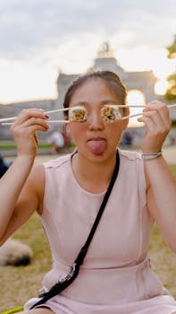 Young girl having fun with sushi and chopsticks in a bright park setting.