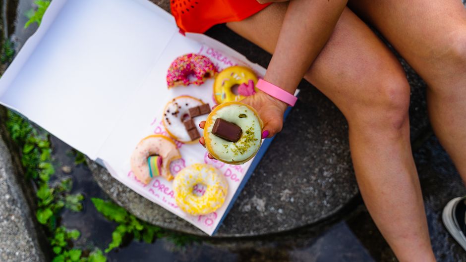 A person holds a decorated doughnut from a colorful assortment in a box outdoors.