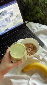 A nutritious breakfast with a laptop, featuring oatmeal, banana, and a glass of green smoothie.