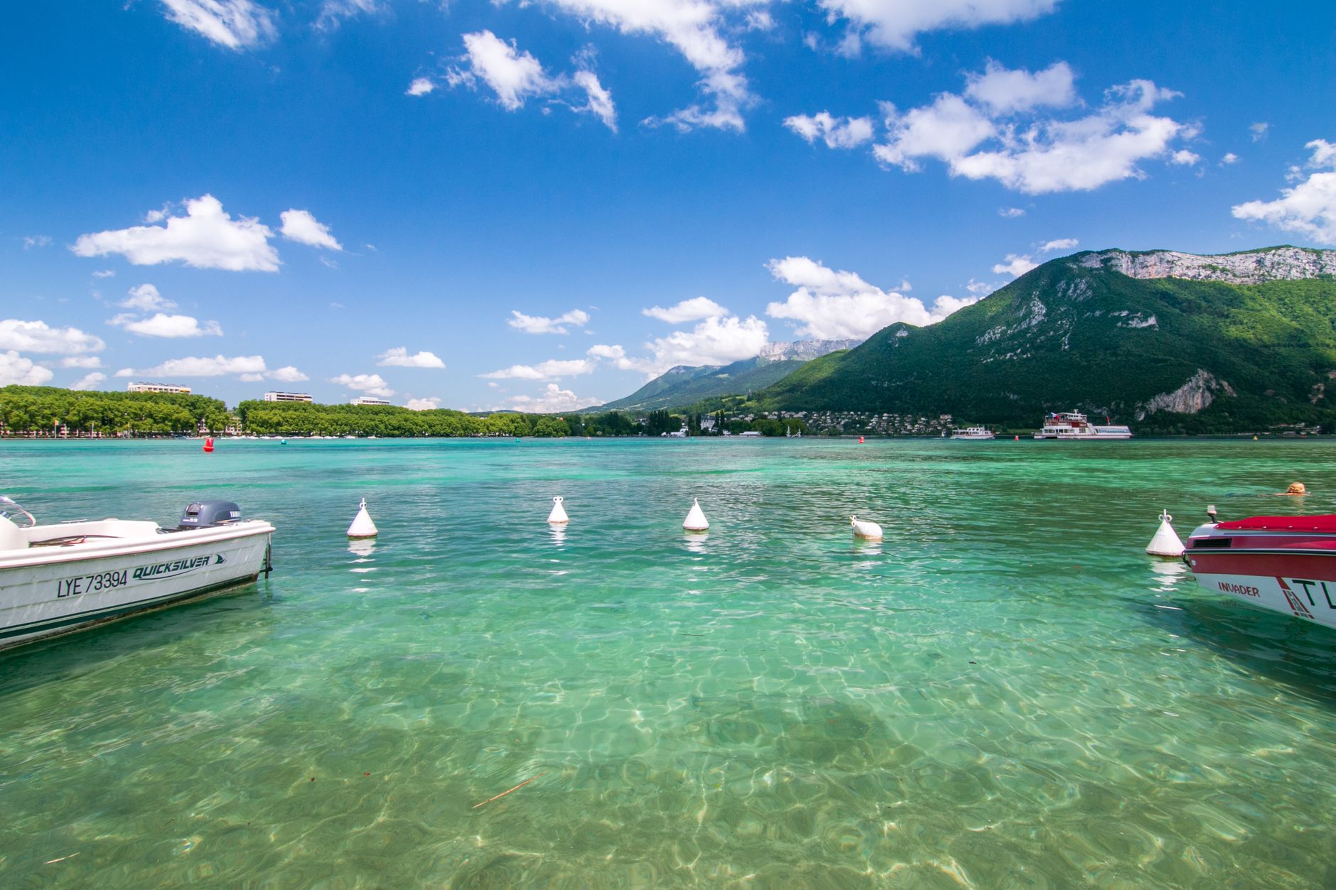 Impresionantes aguas turquesas del lago de Annecy con un hermoso telón de fondo montañoso y lanchas ancladas.