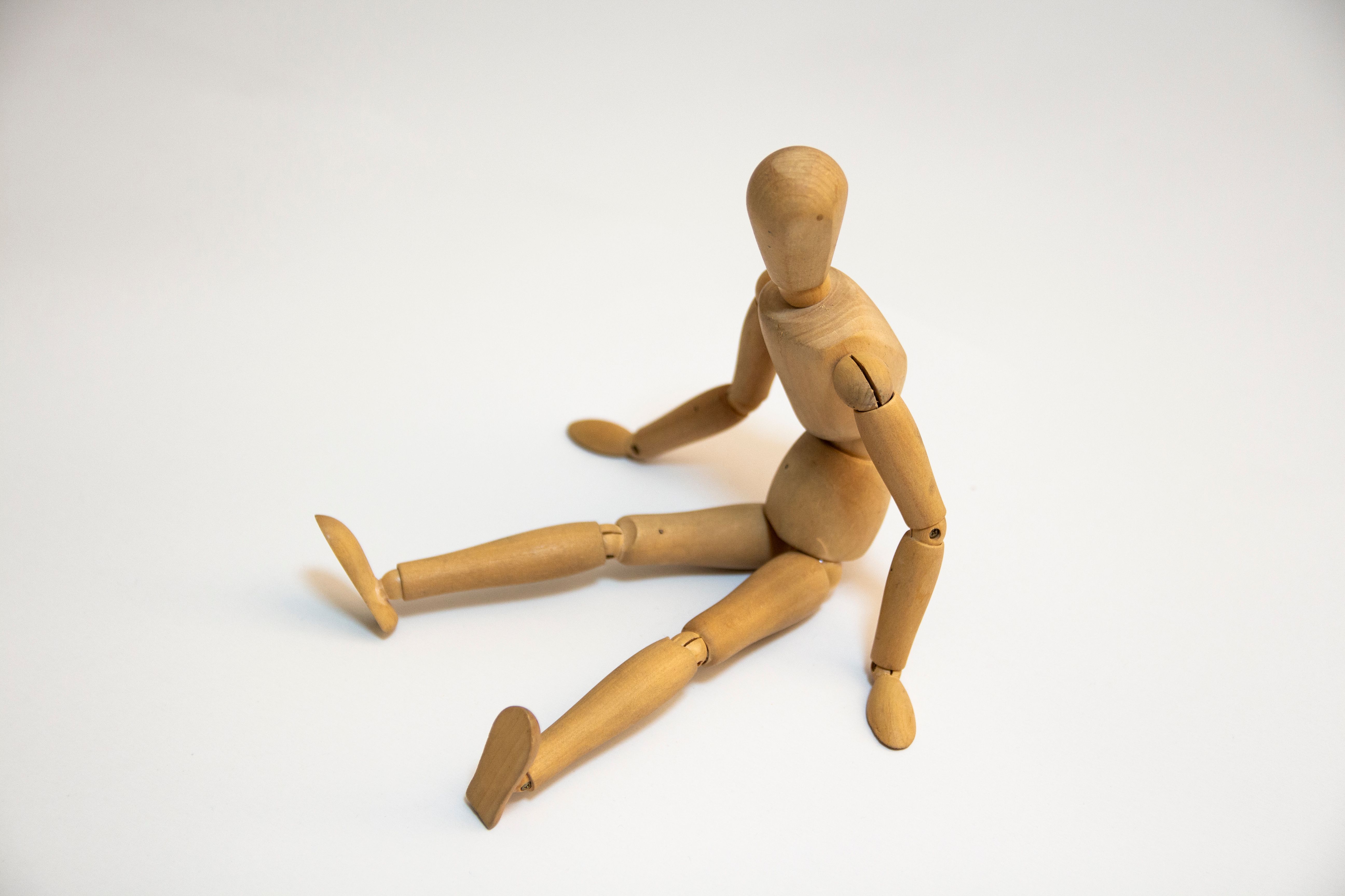 Wooden artist's mannequin seated on a white surface, showcasing flexibility.