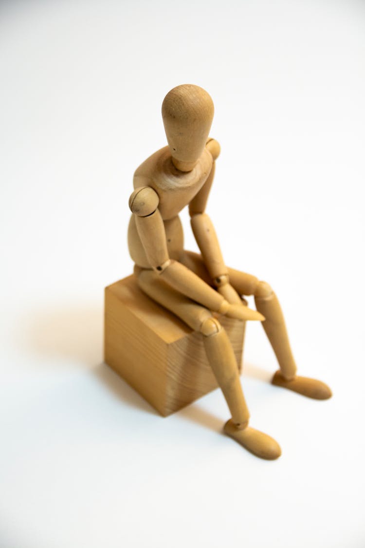 Close-Up Photo Of A Wooden Figurine Sitting On A Block