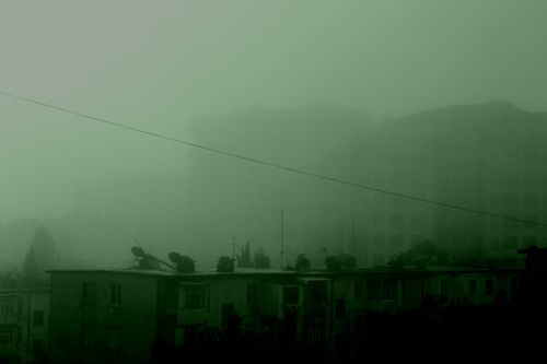 Free A dramatic foggy cityscape in green tones featuring silhouettes of urban buildings. Stock Photo