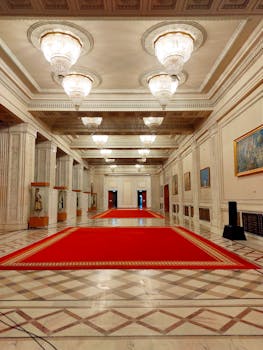 Luxurious interior hallway with a red carpet in a Bucharest palace, featuring grand chandeliers and ornate decor.