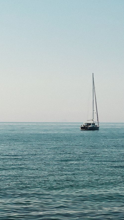 Free A tranquil sailboat drifting on the calm blue ocean under the clear sky, perfect for travel dreams. Stock Photo