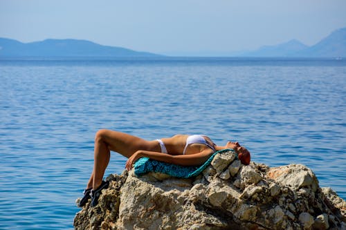 A Woman in White Bikini Lying on the Rock Near the Body of Water