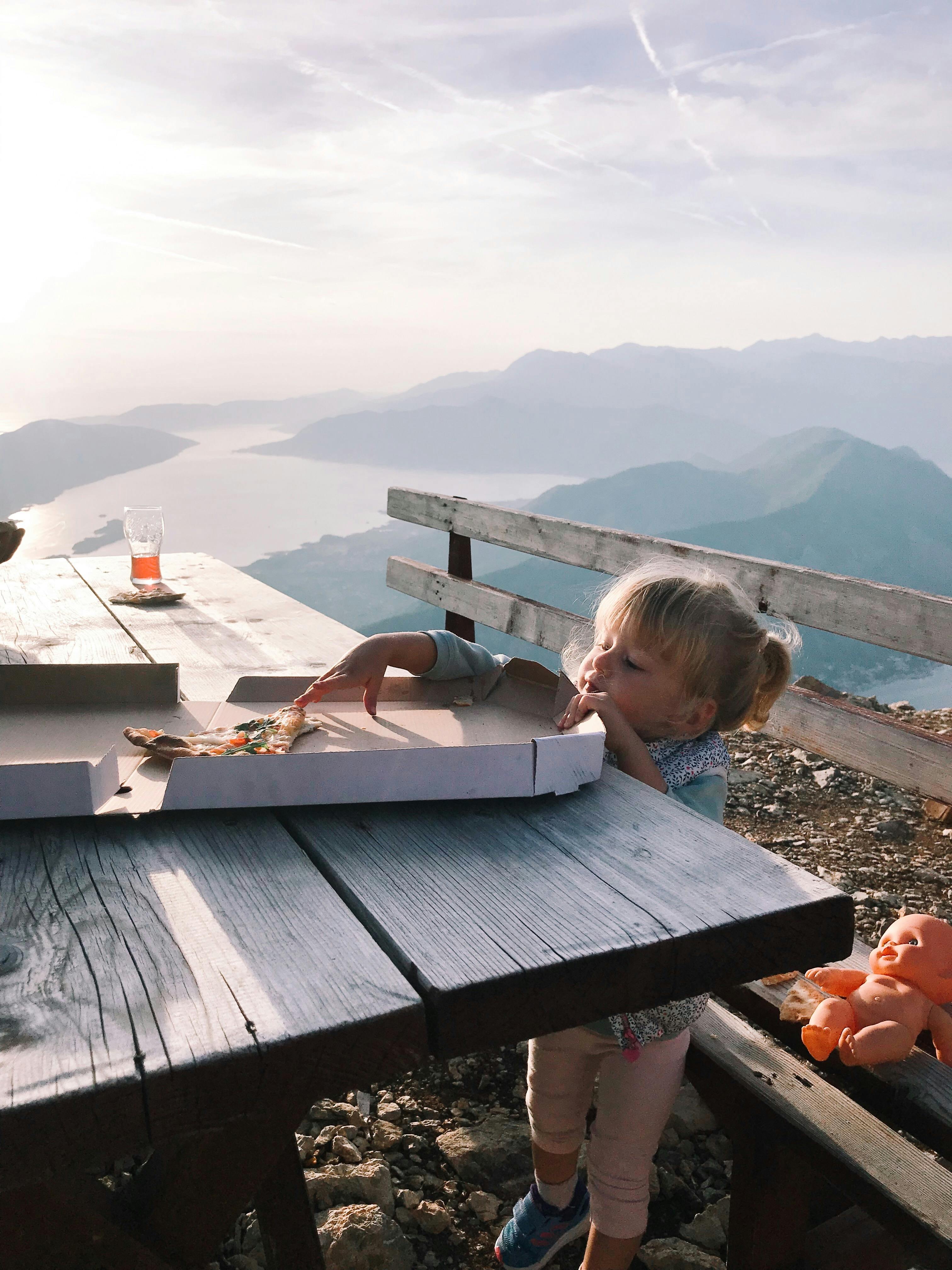 a young girl reaching a pizza on a wooden table