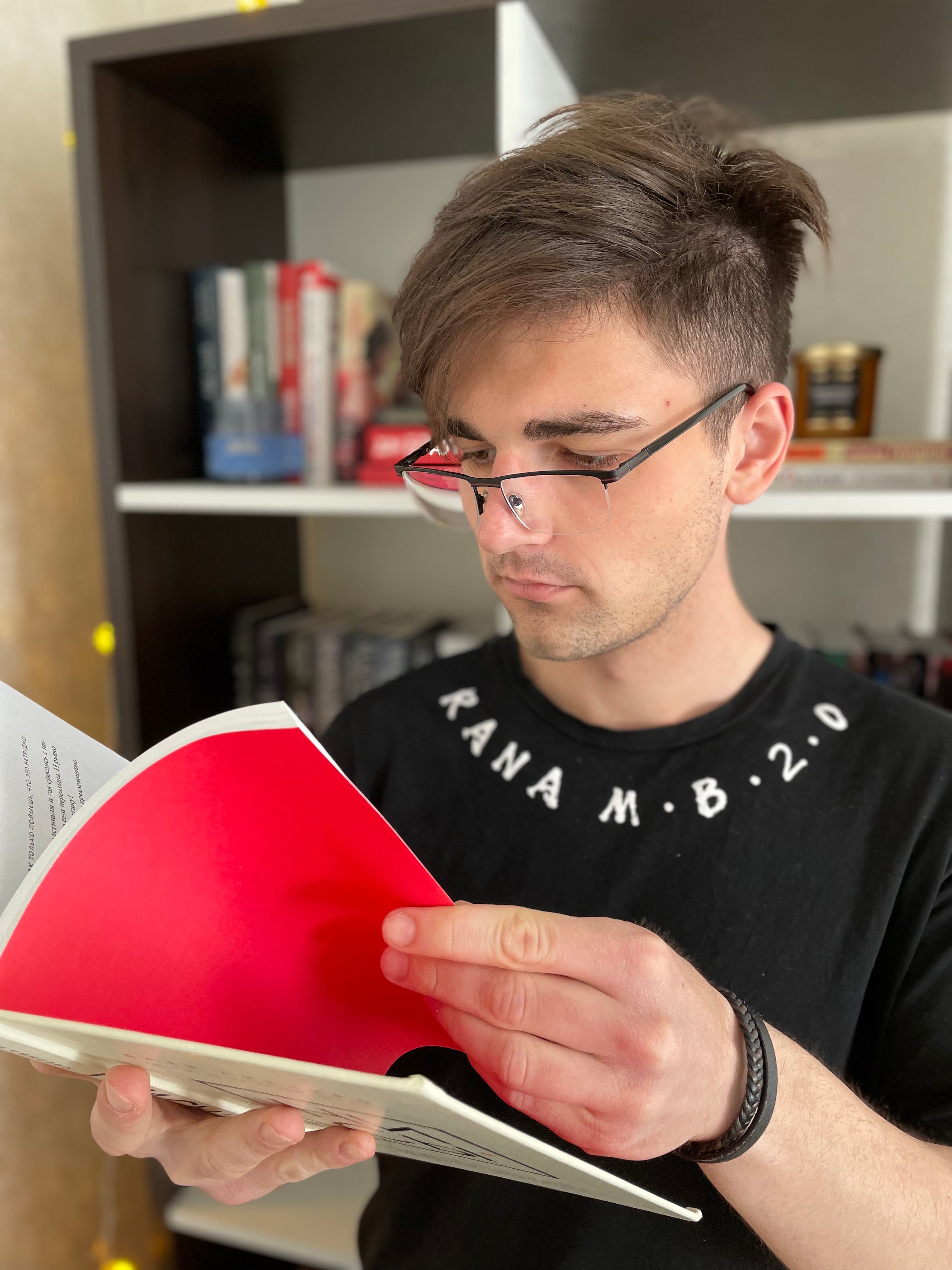 Adult man with eyeglasses reading a book in a contemporary library, emphasizing focus and learning.