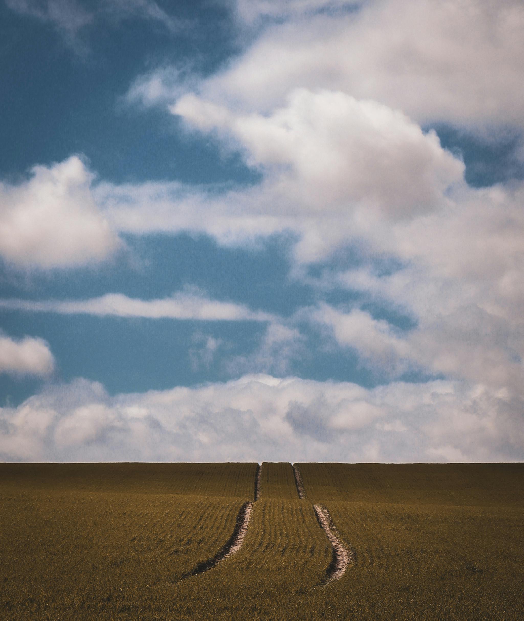 A serene rural landscape showcasing a vast field under a strikingly blue sky with white clouds.
