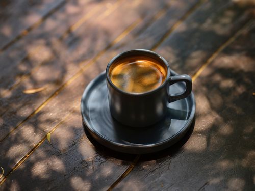 Free A calming scene of a coffee cup on wooden table amidst sunlit shadows. Stock Photo