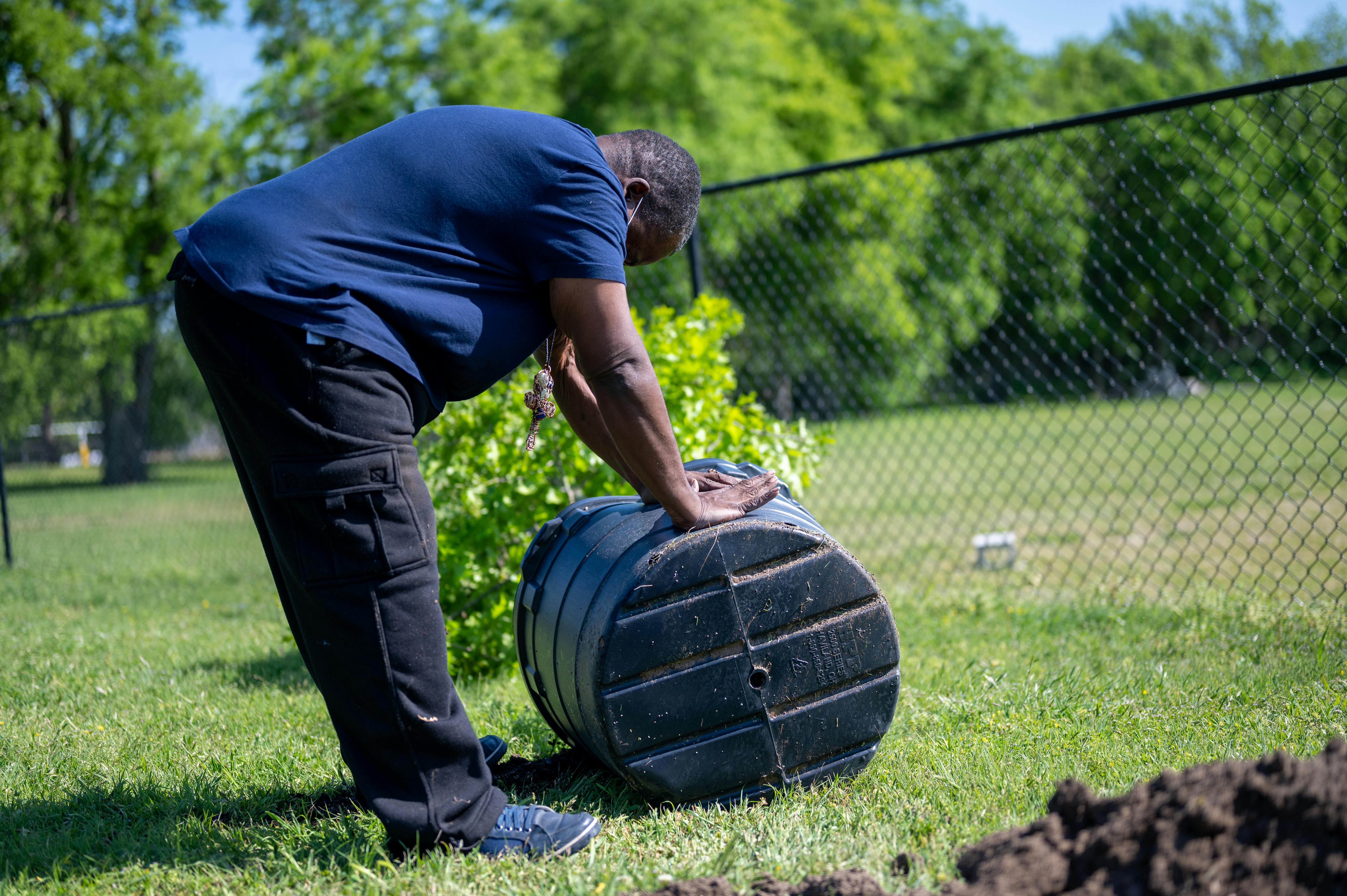 A man working with a compost bin in a sunny park, promoting outdoor gardening activities. Should Compost Bins Be in the Sun or Shade?