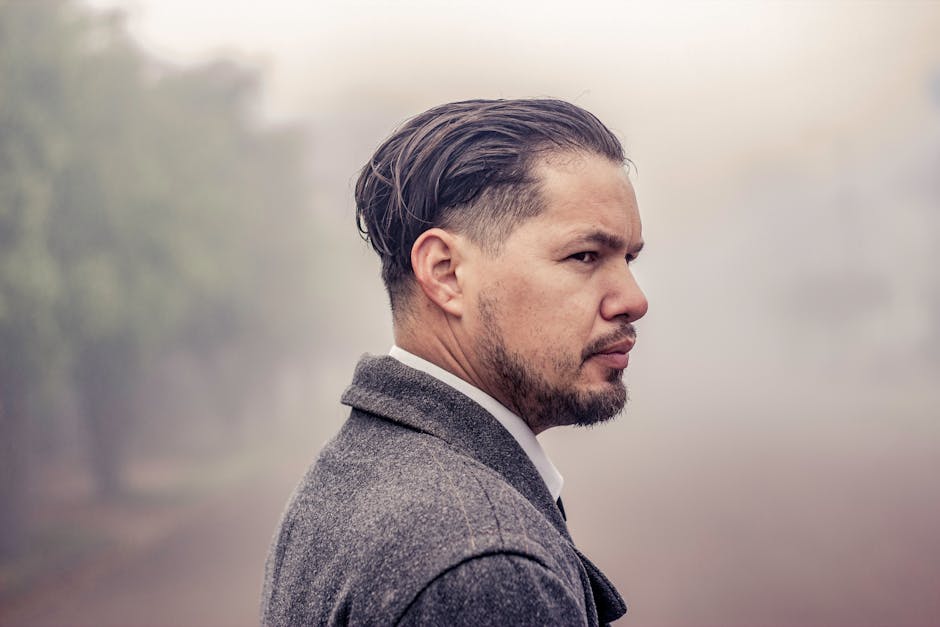 A profile portrait of a man with facial hair in a gray suit amidst a serene foggy background.