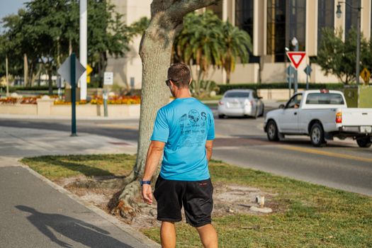 A man in casual attire walks along a city sidewalk on a sunny day.