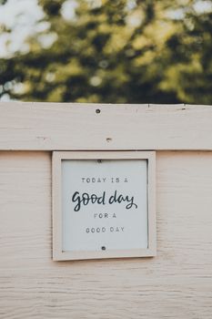 A motivational quote framed on wood against a blurred tree backdrop.