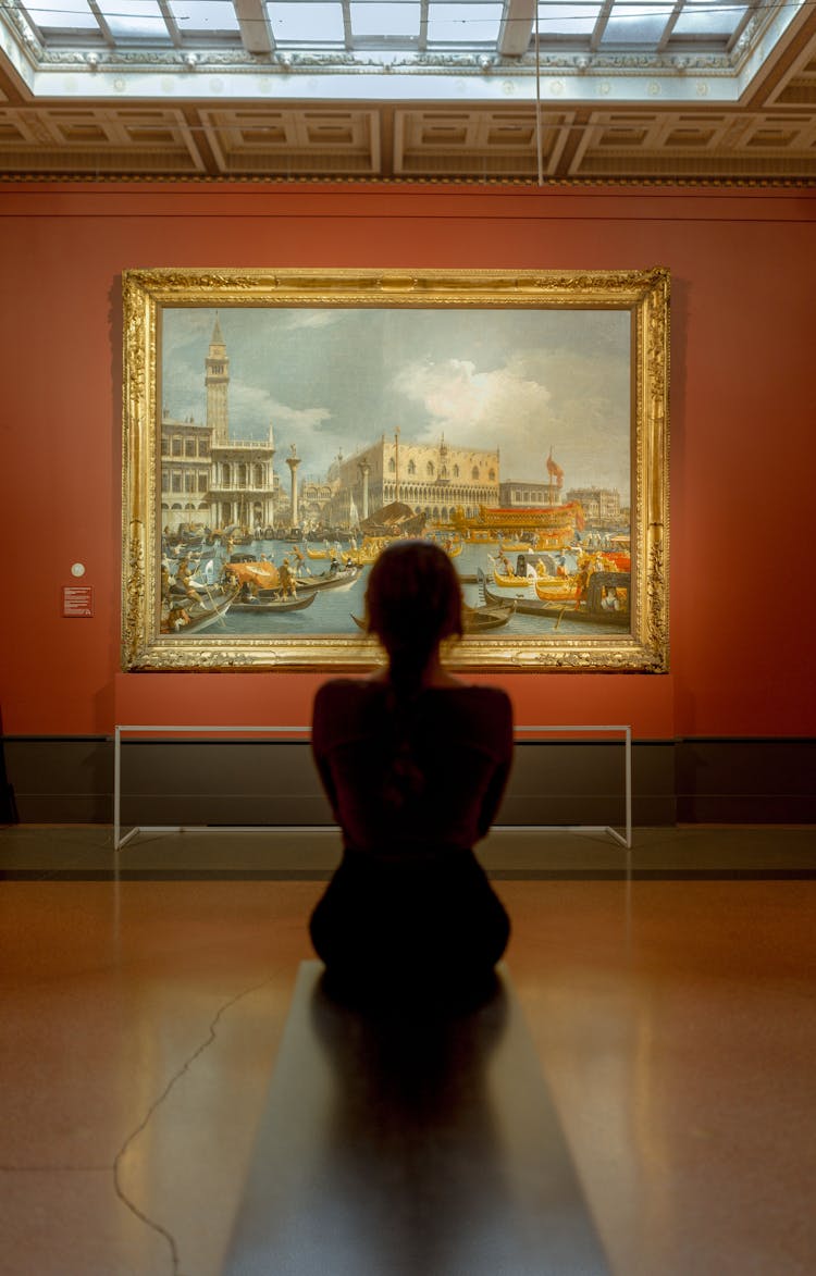 Woman Sitting In Front Of A Painting In A Museum 