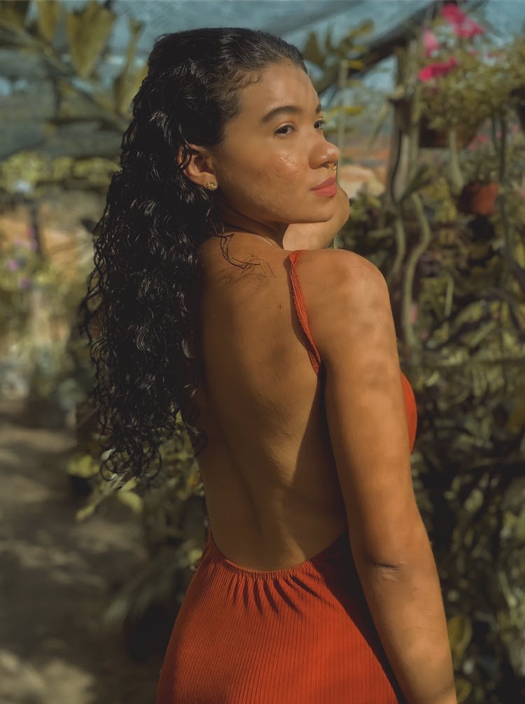 Photo Of A Young Beautiful Woman In A Red Dress Standing Next To Plants