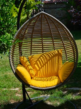 Relax in a stylish hanging egg chair with bright yellow cushions, set in a tranquil garden.
