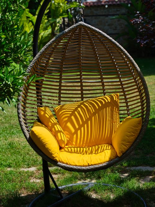 Free Relax in a stylish hanging egg chair with bright yellow cushions, set in a tranquil garden. Stock Photo
