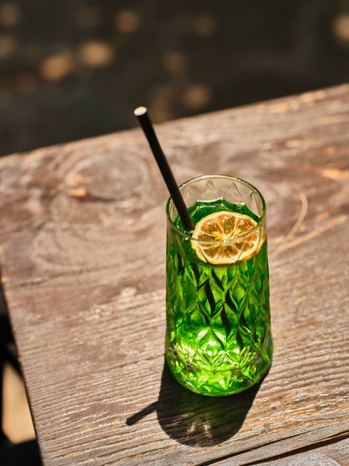 Free Close-up of a vibrant green cocktail with a lime slice and straw on a wooden table. Stock Photo
