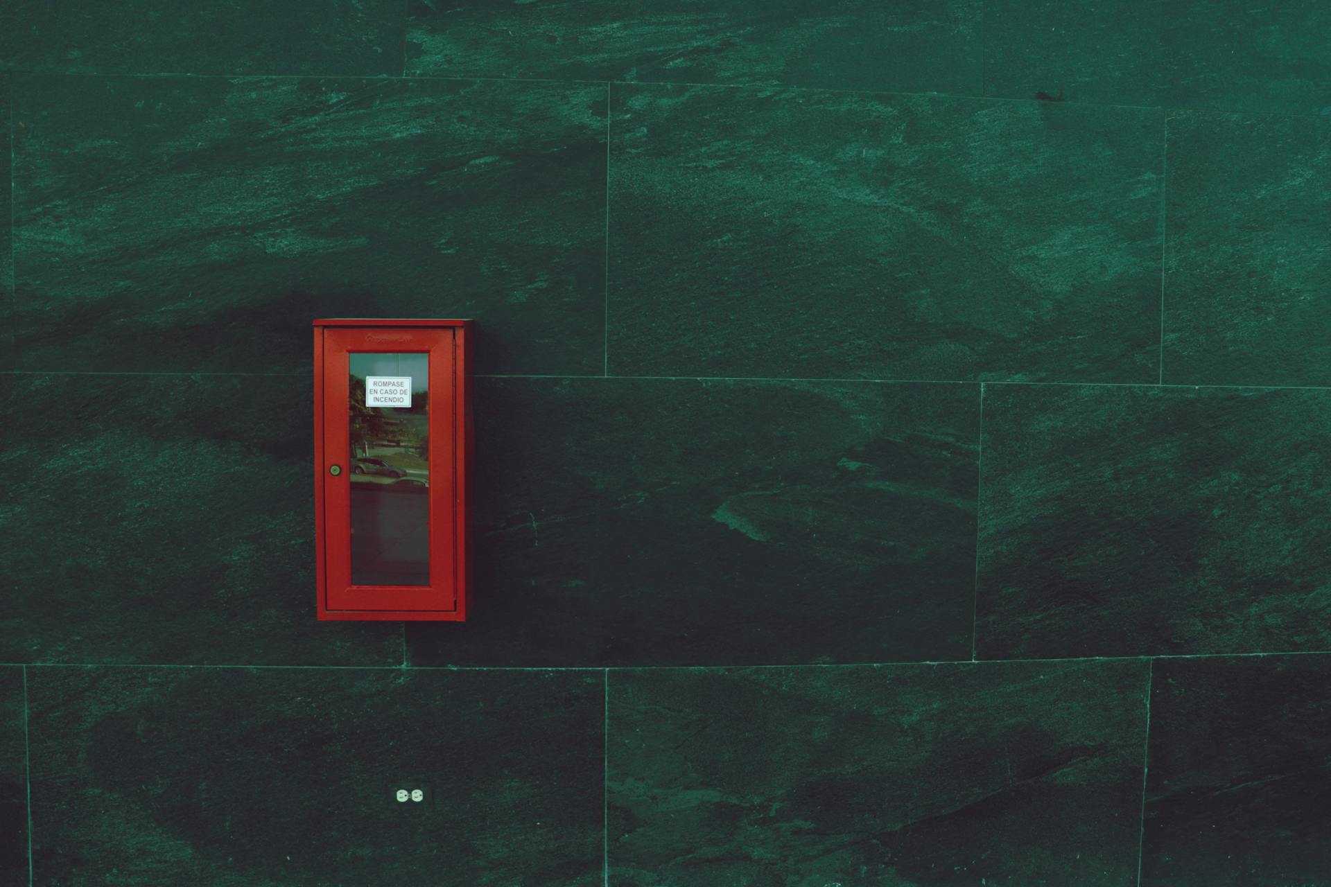 Red emergency box mounted on a dark textured wall, showcasing minimalist design.