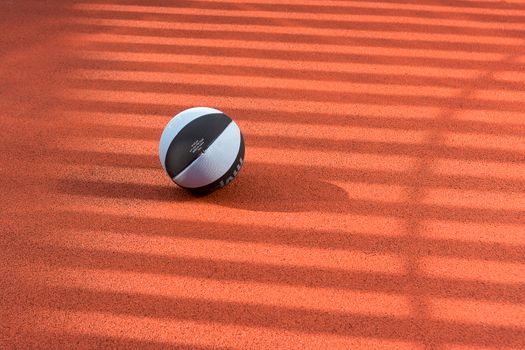 A black and white basketball sits on a sunlit court with shadow stripes, creating an artistic effect.