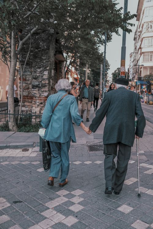 Free A senior couple holds hands while crossing a city street, capturing a moment of companionship. Stock Photo