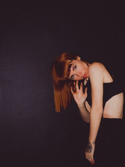 Free Stylish portrait of a red-haired woman posing in a black outfit with a dark backdrop, exuding elegance and fashion. Stock Photo