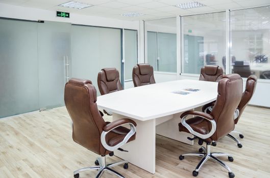 Spacious conference room with modern design, featuring leather chairs and a white table.