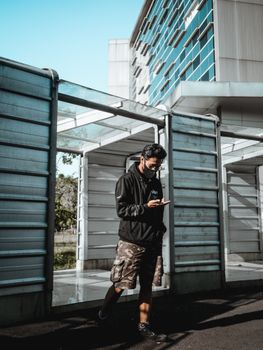 Person in a black hoodie and face mask walking past modern architecture safely.