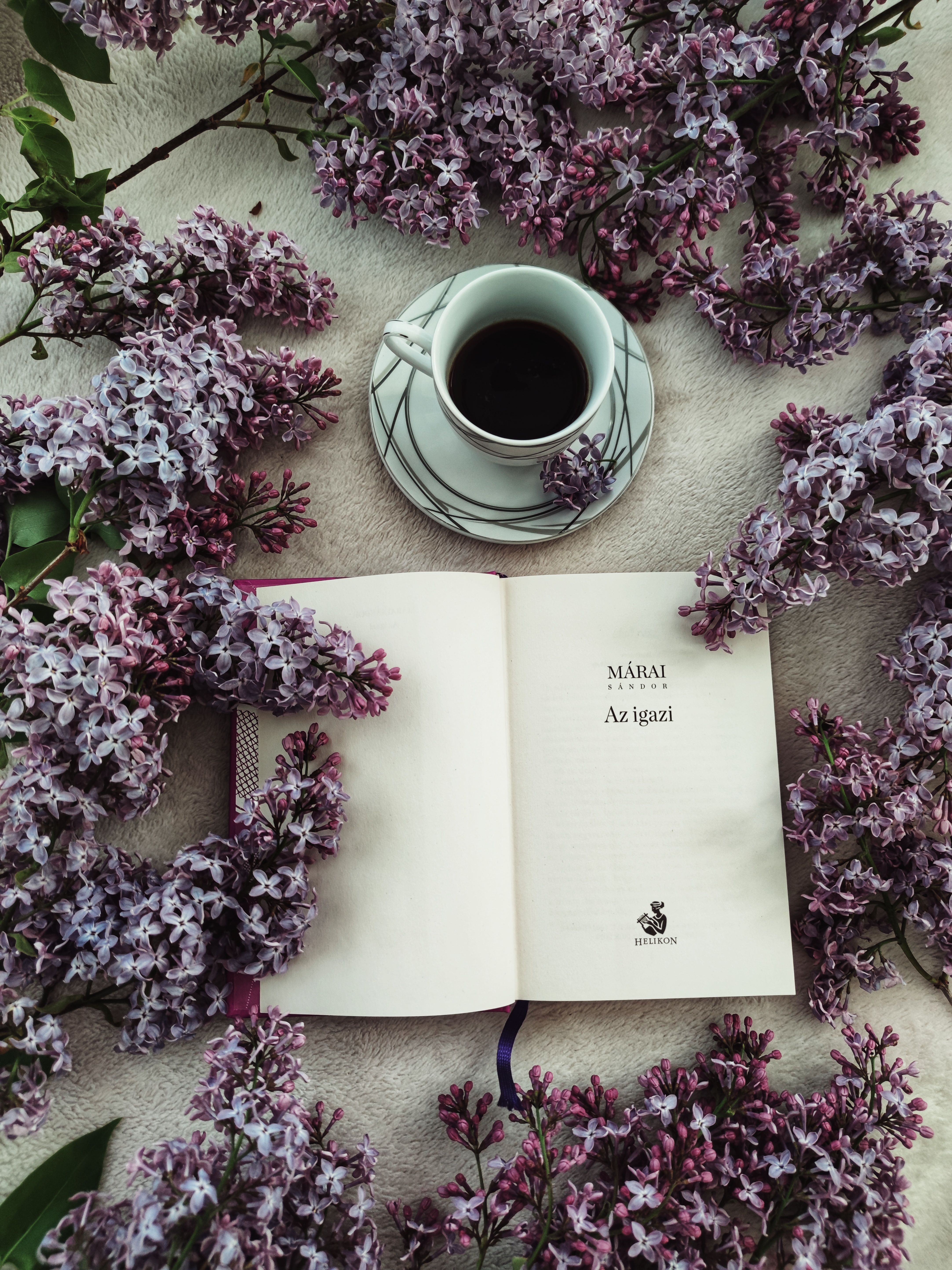Cup of coffee next to an open book surrounded by lavender flowers, top view.