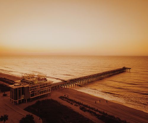 Free Wooden pier extending into the ocean at sunset with warm, earthy tones and empty beachfront. Stock Photo