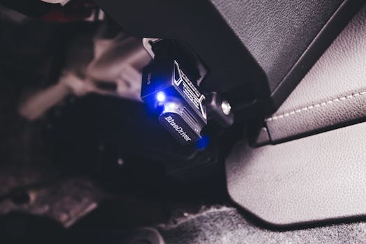 Close-up of a Bluetooth code reader tool connected inside a vehicle, illuminated by a blue light.