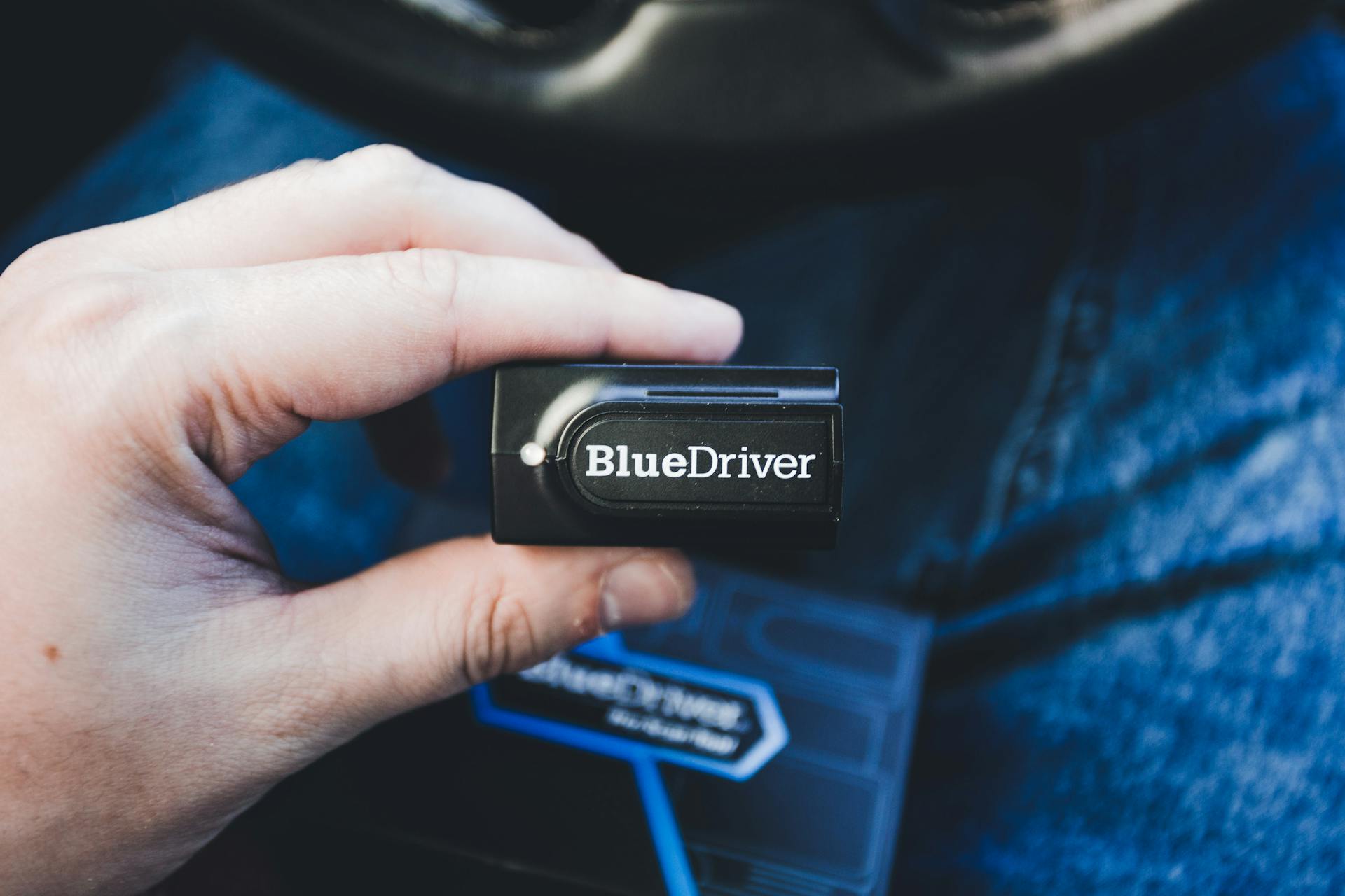 A person holding a portable car diagnostic tool in a vehicle environment.