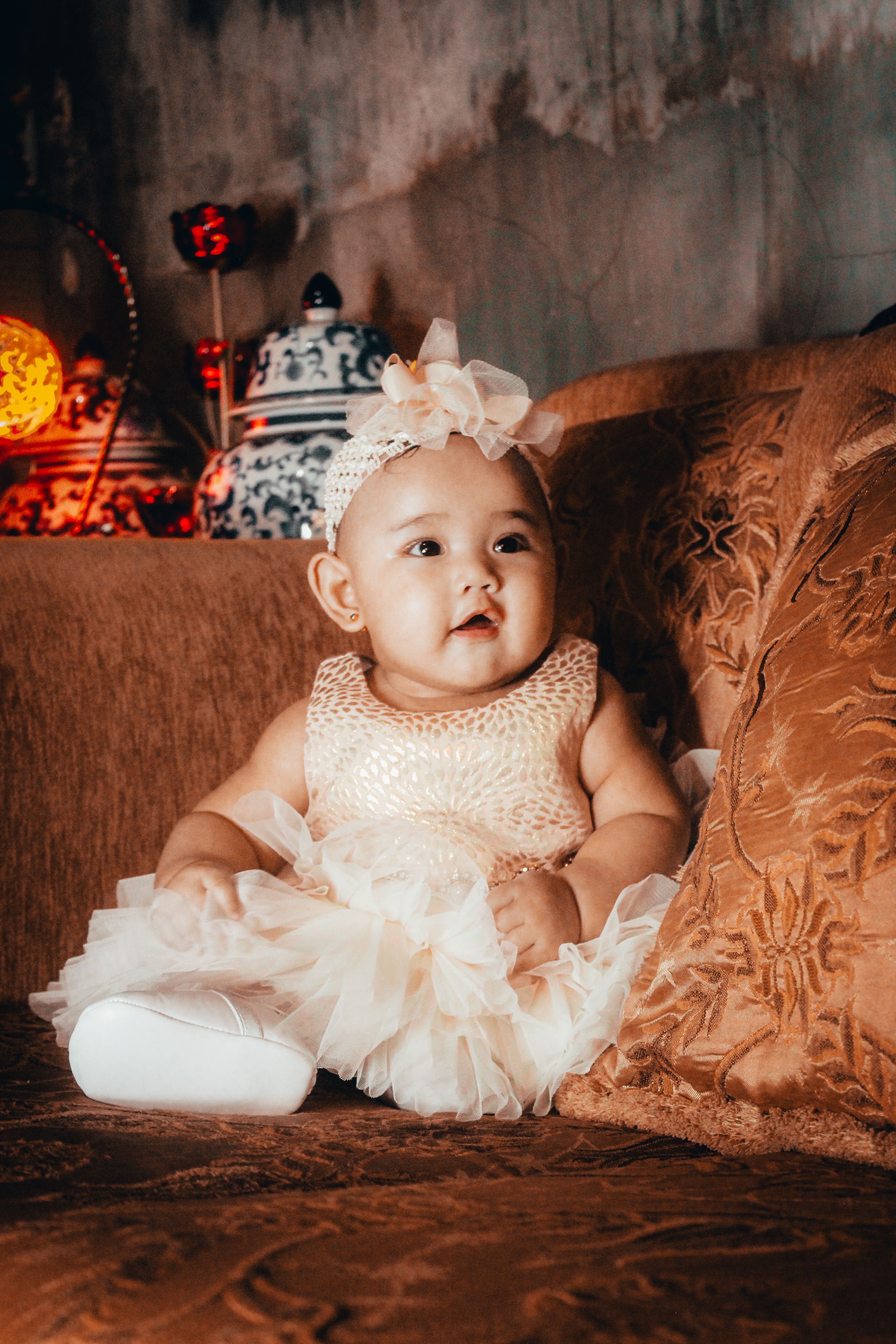 Baby in White Dress Sitting on Brown Sofa · Free Stock Photo