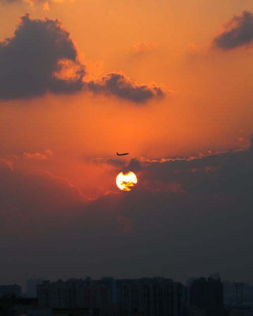 Free A stunning silhouette of an airplane flying over Dubai at sunset, with a vibrant orange sky. Stock Photo