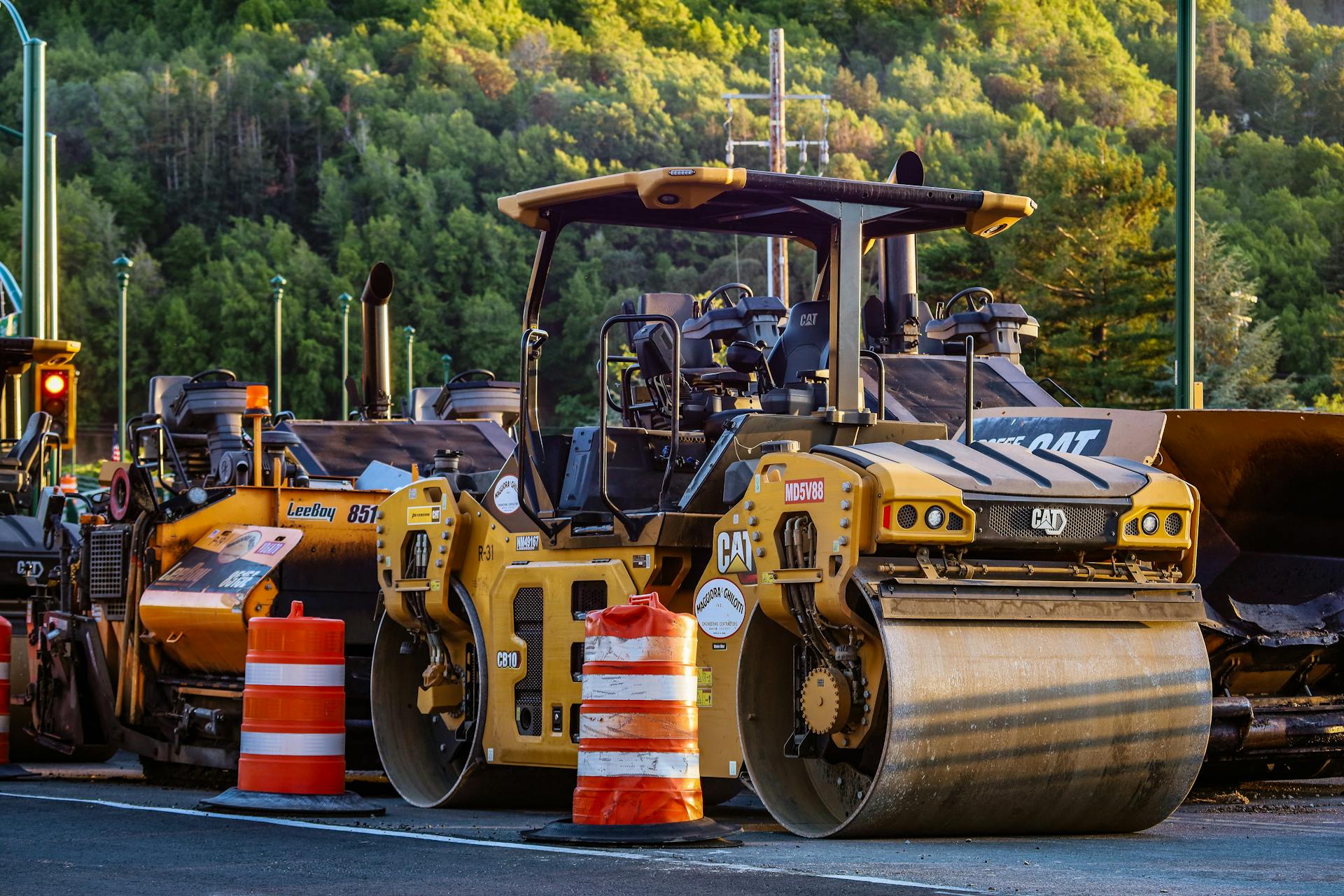 Construction machinery and vehicles on site with road rollers and cones.