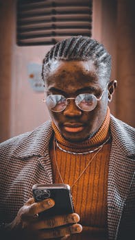 Close-up of a stylish man in glasses using a smartphone, wearing a checkered coat and turtleneck.