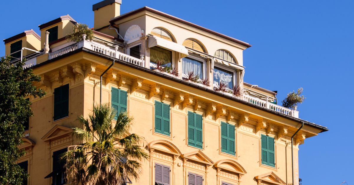 Luxurious yellow building with green shutters and palm tree under a clear blue sky.