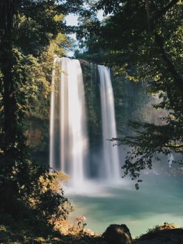 Majestic waterfall cascading amidst a verdant forest, creating a tranquil natural scene.