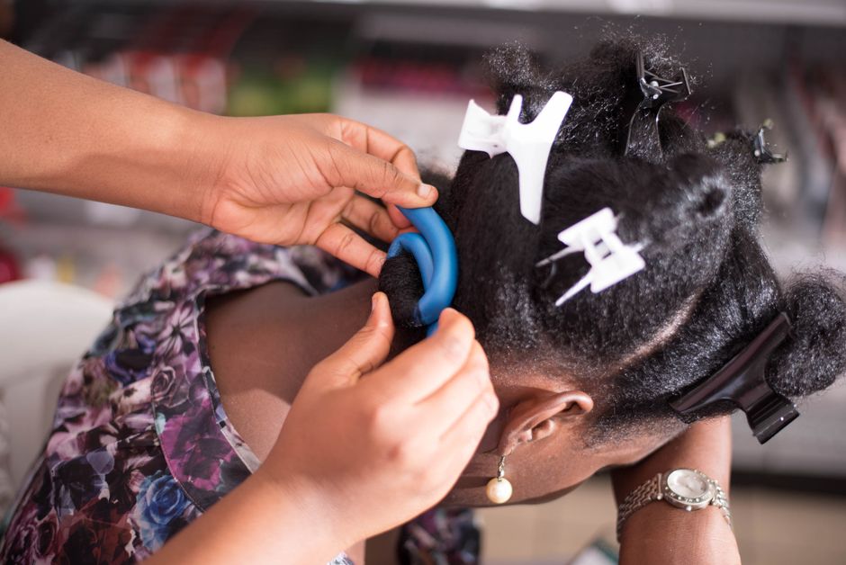 Close-up of hairstyling with clips and curlers on afro hair, focusing on detail.