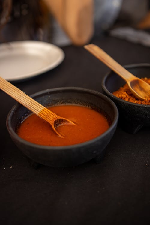 Free A Red Spicy Soup with Wooden Spoon in a Black Bowl Stock Photo